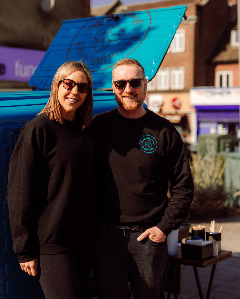 Charlie and Abbi, founders of Roaming Roast, beside their blue Piaggio Ape coffee van